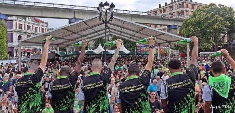 Varios participantes en el concurso de escanciadores escancian sidra simultáneamente. El público contempla el escanciado.