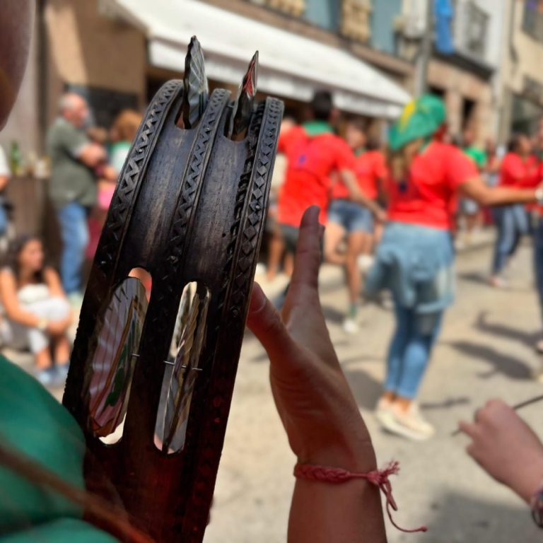 Una mano toca una pandereta en primer plano y unas personas bailan al fondo.